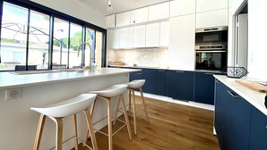 Eine moderne Küche mit Kochinsel, Barhocker und Blick ins Freie.