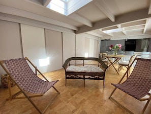 A room with a high ceiling, a wicker sofa, two lounge chairs, a dining table with chairs, and a kitchen area in the background. - Complete outbuilding in La Teste town centre (La Teste-de-Buch)