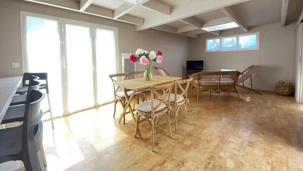 Una habitación amplia con una mesa de madera, sillas, un televisor y un ventanal grande.