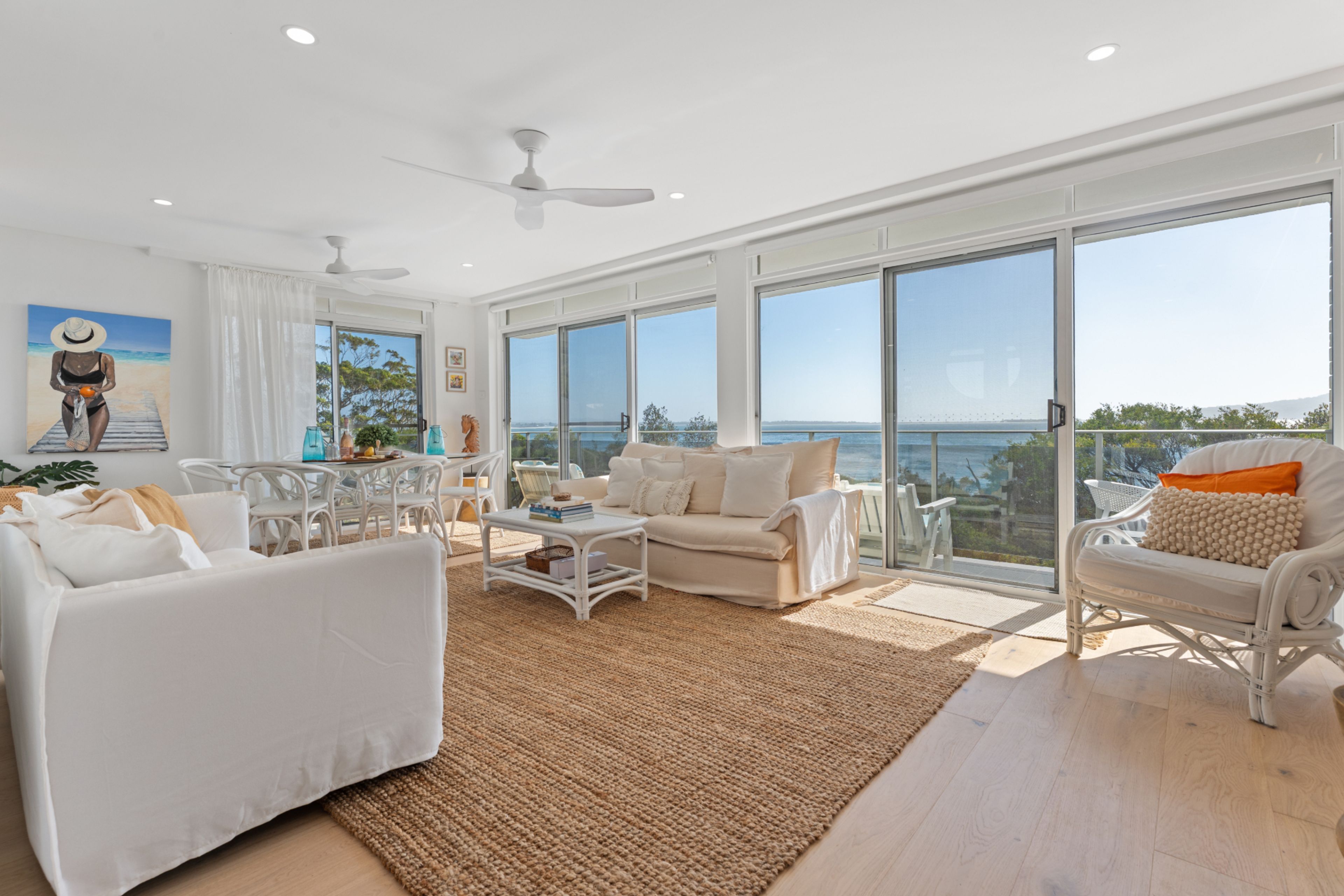 A spacious living room with a large window, a ceiling fan, and a view of the ocean.