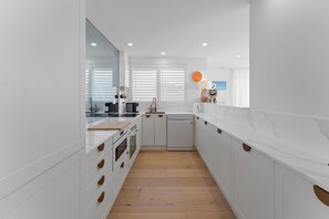A modern kitchen with white cabinetry, a wooden countertop, and a view of the beach through the window. - Beachfront at Shoal Bay (Nelson Bay)