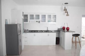 A modern kitchen with white cabinets, a stainless steel refrigerator, a sink, and a small island with stools.