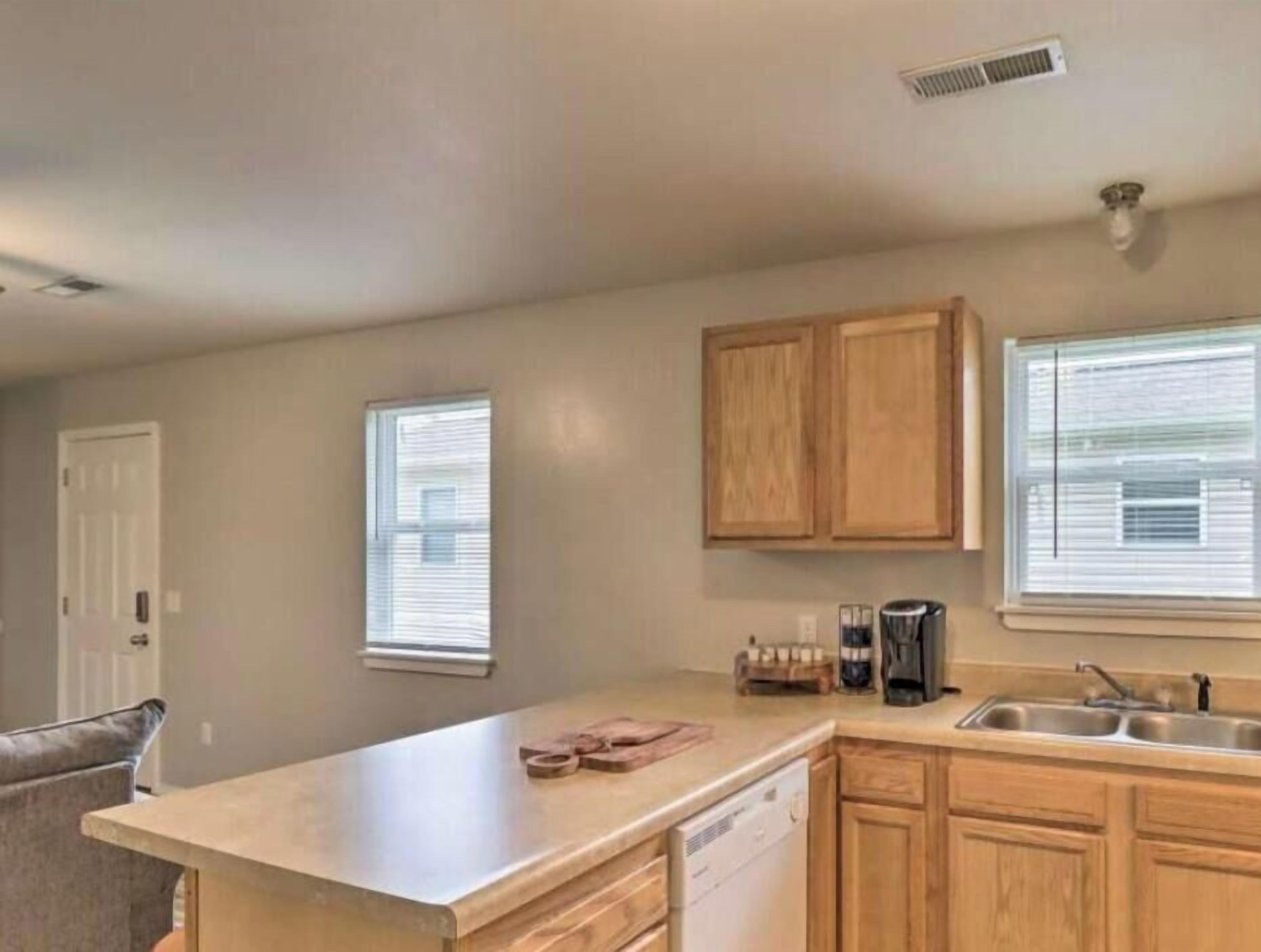A kitchen with wooden cabinets, a dishwasher, a coffee maker, and a window with blinds.