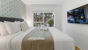 Une chambre à coucher avec un lit, des oreillers, une couverture, une fenêtre et un tableau.