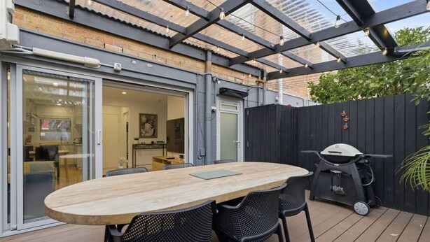 Une terrasse extérieure avec une table et des chaises en bois, un barbecue et un espace couvert d’où l’on peut admirer l’intérieur.