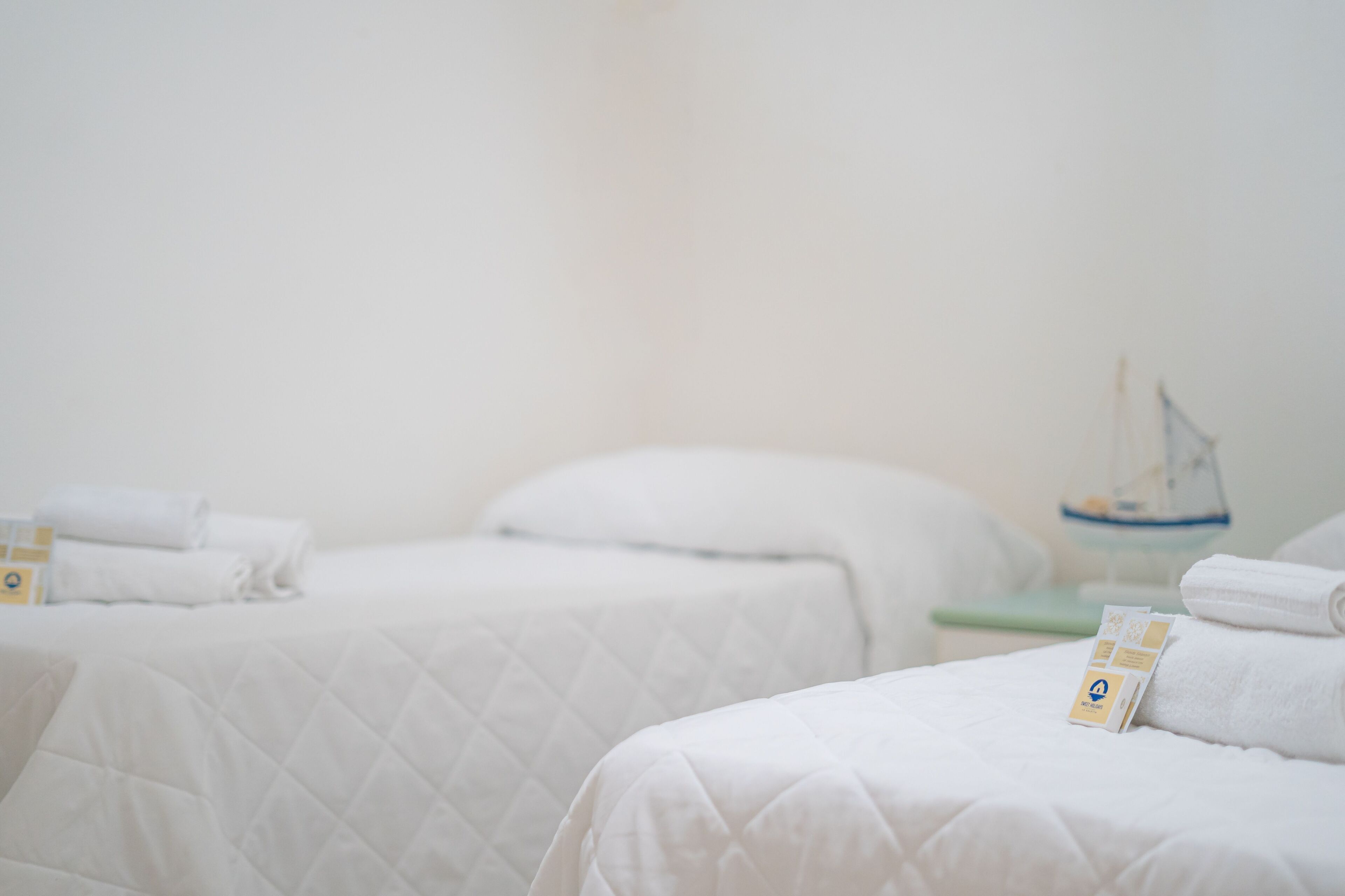 Two beds with white linens, a small table with a sailboat decoration, and a green chair.