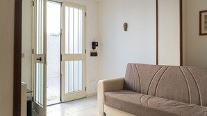Ett rum med en beige soffa, en skjutdörr i glas som leder ut, en väggmonterad ljusströmbrytare och en liten tavla i en ram.