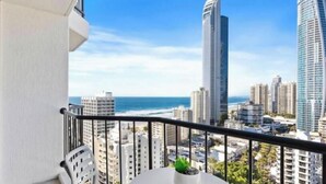 Ein Balkon mit weißem Tisch und Stuhl, einem Blumentopf und Blick auf die Stadt mit hohen Gebäuden und dem Meer.
