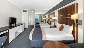 Ein Hotelzimmer mit Schreibtisch, zwei Betten, Fernseher und Blick auf die Stadt.