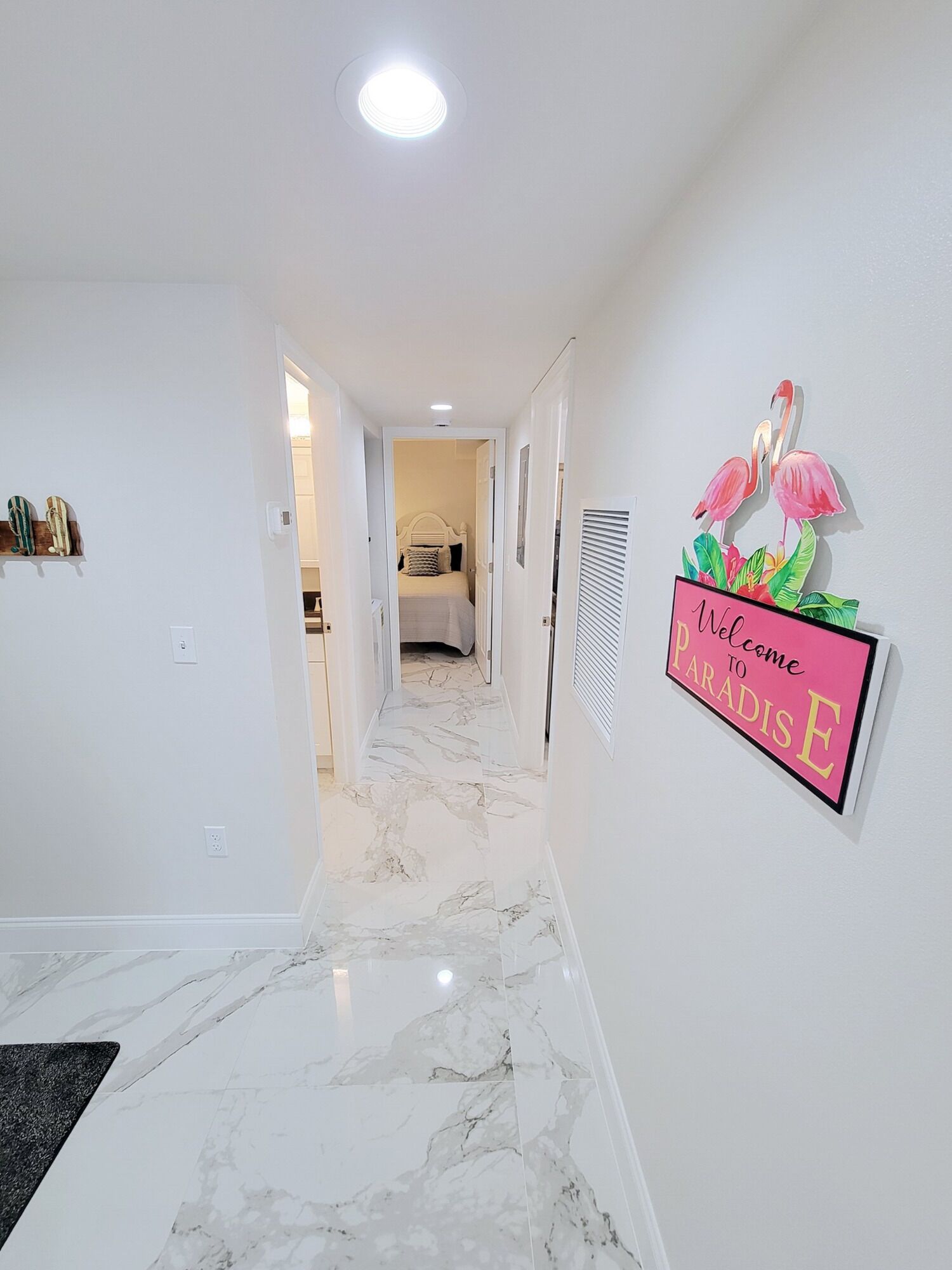A hallway with a marble floor, a bed in the background, and a welcome sign on the wall.