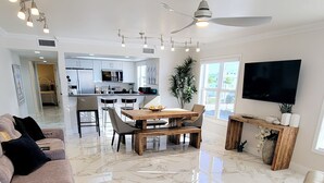 Uma sala de estar moderna com piso de mármore, uma mesa de jantar de madeira, um sofá, uma televisão e um ventilador de teto.