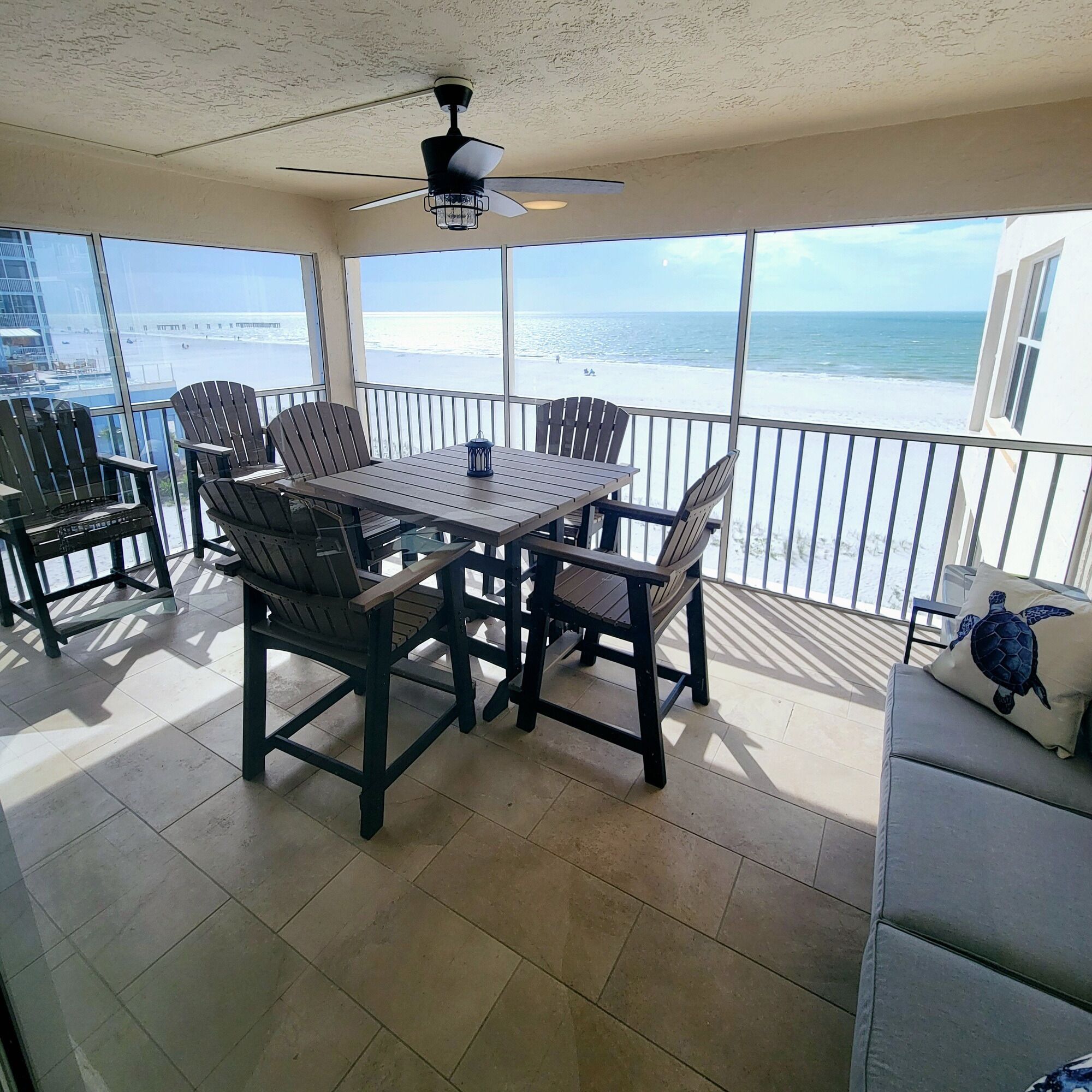 A balcony with a table and chairs, a ceiling fan, and a view of the beach.