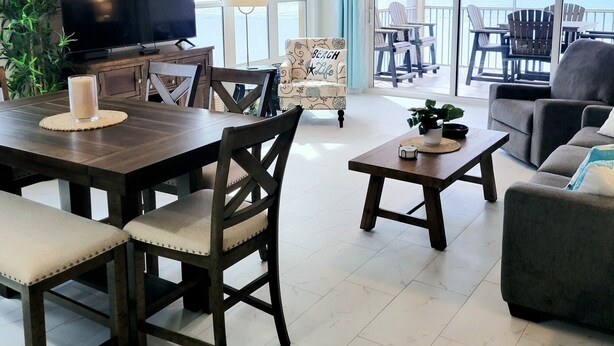 Un vaste espace de vie comprenant une table à manger, des chaises, un canapé, un téléviseur et un balcon avec des sièges d’extérieur.