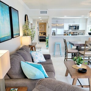 Ein modernes Wohnzimmer mit grauem Sofa, einem Esstisch und einer Küche im Hintergrund.