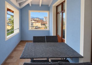 Un balcó amb taula i cadires, una finestra amb vista a edificis i muntanyes, i un terra de rajoles.
