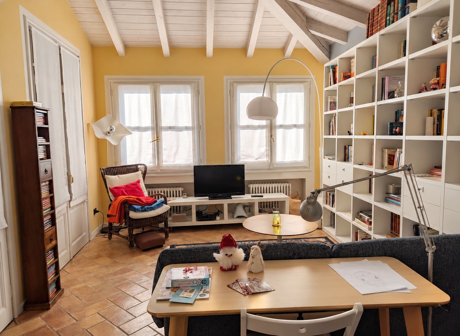 Ein gemütliches Wohnzimmer mit Fernseher, Bücherregalen, einem Esstisch mit Papieren und einer Couch.