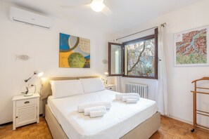 Ein ordentlich eingerichtetes Schlafzimmer mit Bett, Nachttischen, einem Fenster mit Aussicht und einer Wand-Klimaanlage.
