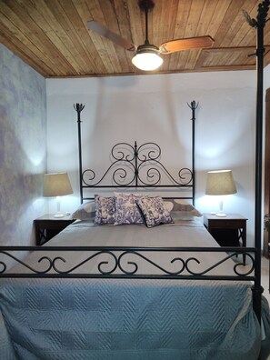Une chambre à coucher avec un lit à baldaquin, deux tables de chevet avec des lampes, un ventilateur de plafond et un plafond en bois.