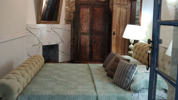 Ein Schlafzimmer mit Bett, Deckenventilator, Steinwand, Holztür und Spiegel.