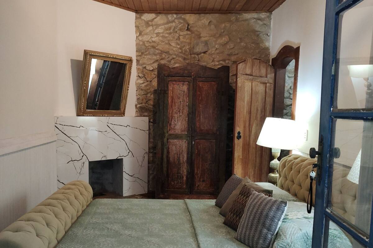 Une chambre à coucher avec un lit, un ventilateur de plafond, un mur en pierre, une porte en bois et un miroir.