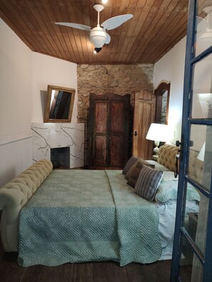 Une chambre à coucher avec un lit, un ventilateur de plafond, un mur en pierre, une porte en bois et un miroir.