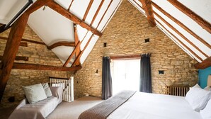 Ein Schlafzimmer mit Steinwand, Holzbalken, einem Bett, einer Bank und einem Fenster mit Vorhängen.