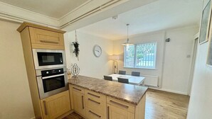 Una cocina con armarios de madera, encimera de granito, horno empotrado y comedor con mesa y sillas.