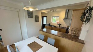 Cocina compacta con una isla central, zona de comedor con mesa blanca y un pequeño ventanal que aporta luz natural.