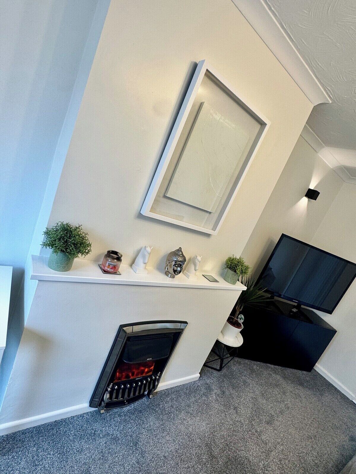 A modern living room with a fireplace, a mounted TV, and a shelf with decorative items.