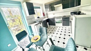 A compact kitchen with a washing machine, a dining area with two chairs, and a patterned floor. - Homely 2 bedroom house, parking (Kidlington)