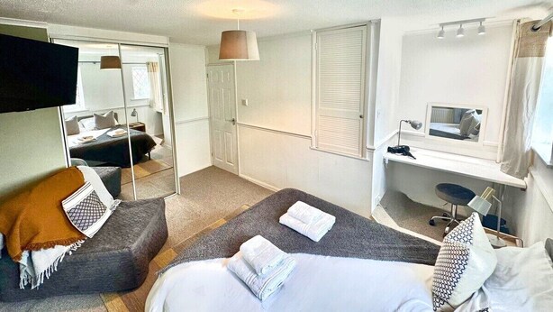 A compact hotel room with a bed, a desk, a chair, a mirror, and a wardrobe. - Homely 2 bedroom house, parking (Kidlington)