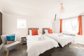 Quarto de hotel com duas camas, uma escrivaninha, uma cadeira e uma janela com cortinas.