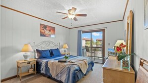 A bedroom with a bed, two bedside tables, a ceiling fan, a balcony with a view, and a desk with a lamp. - Inlet Point Villas 11D - Pool View (North Myrtle Beach)