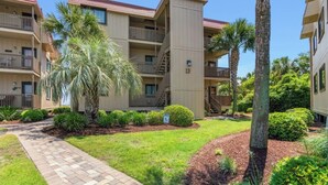 A multi-story residential building with balconies, a paved walkway, and landscaped greenery. - Inlet Point Villas 11D - Pool View (North Myrtle Beach)