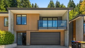 A modern two-story house with a garage, large windows, and a balcony. - Forest Creek Lodge– Mountain Views & Spa Pool (Queenstown)