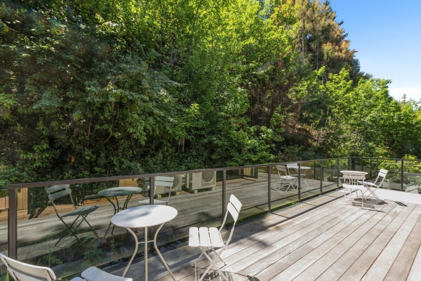 An outdoor deck with tables and chairs, surrounded by dense greenery.