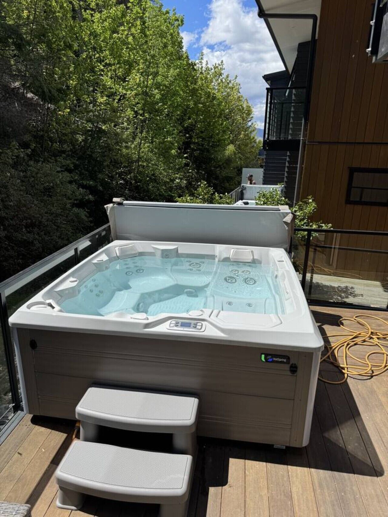 Un bain à remous doté d’un panneau de commande, de deux petits tabourets et d’une terrasse en bois.