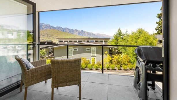 A balcony with wicker chairs, a barbecue grill, and a view of mountains. - Forest Creek Lodge– Mountain Views & Spa Pool (Queenstown)