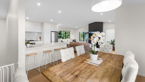 A modern kitchen with white cabinetry, a wooden dining table, and bar stools. - Forest Creek Lodge– Mountain Views & Spa Pool (Queenstown)