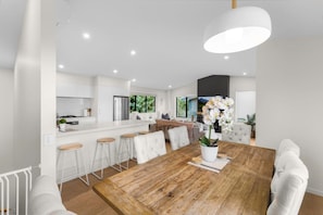 A modern kitchen with white cabinetry, a wooden dining table, and bar stools. - Queenstown Forest Lodge, 4BR Retreat with Spa Pool, Views, Games & Family Comfort (Queenstown)