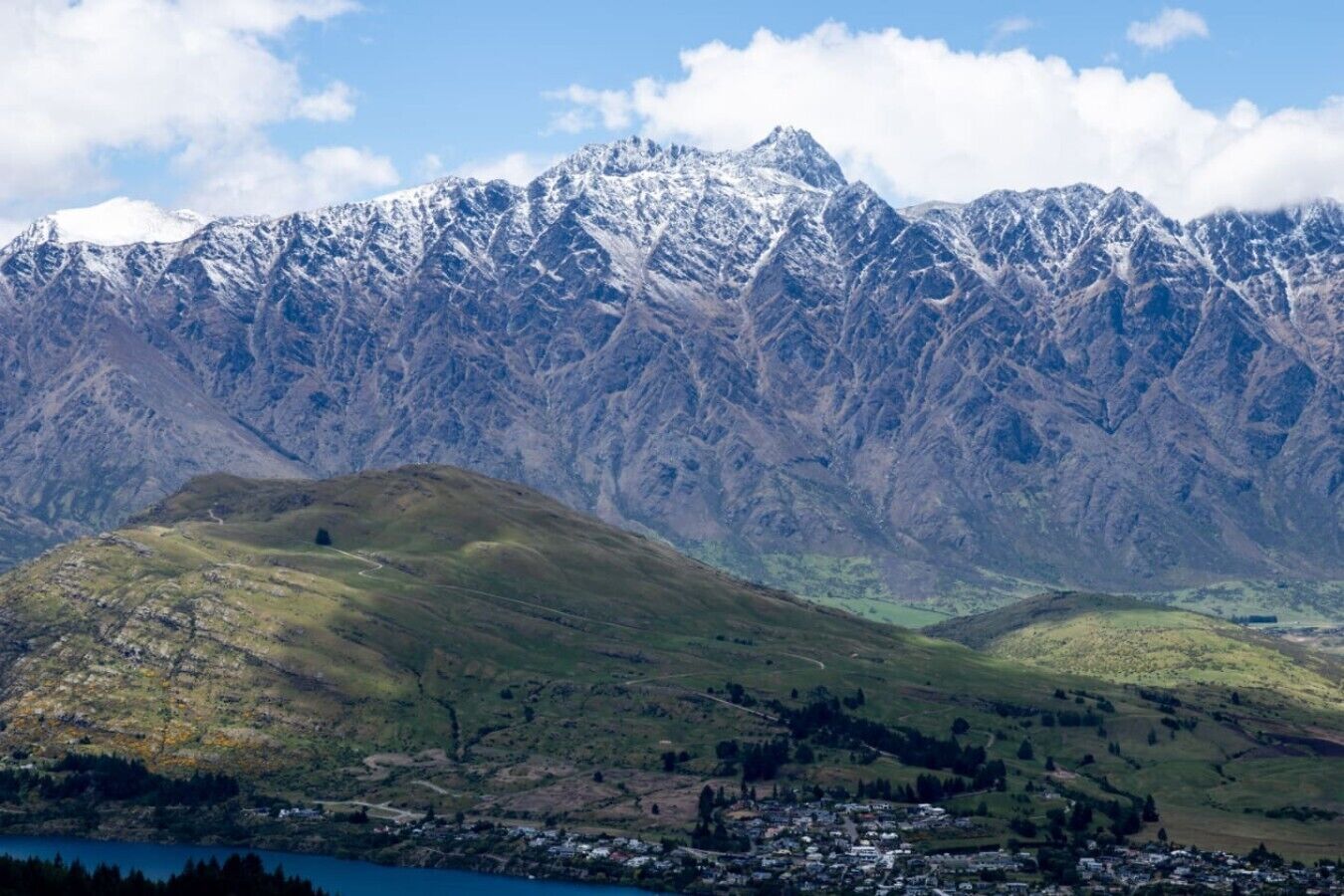 Un paisaje montañoso con un pueblo a los pies, con terreno accidentado y picos nevados.