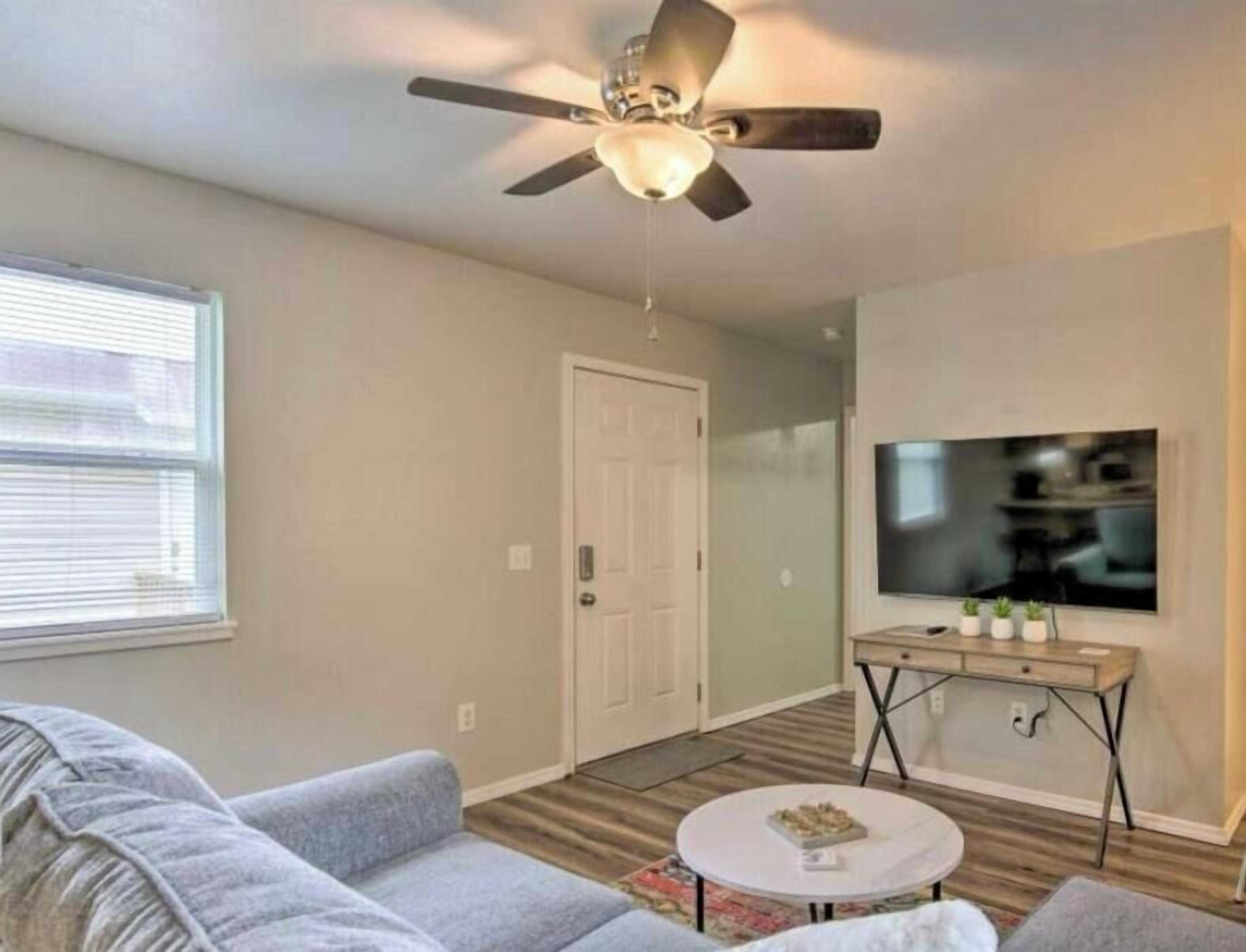 A living room with a ceiling fan, a television, a sofa, a coffee table, and a door.