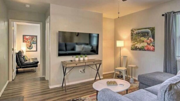 Een woonkamer met een plafondventilator, een flatscreen-tv, een bank, een salontafel en een schilderij aan de muur.