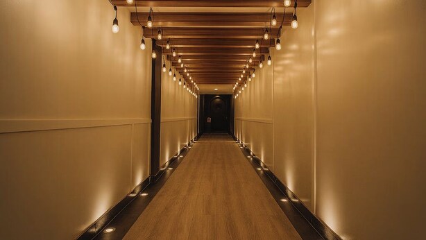 A long, narrow hallway with wooden ceiling beams and hanging light fixtures.
