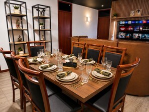 A dining area with a wooden table set for six, surrounded by wooden chairs.