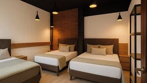 A hotel room with three beds, wooden headboards, and pendant lighting.