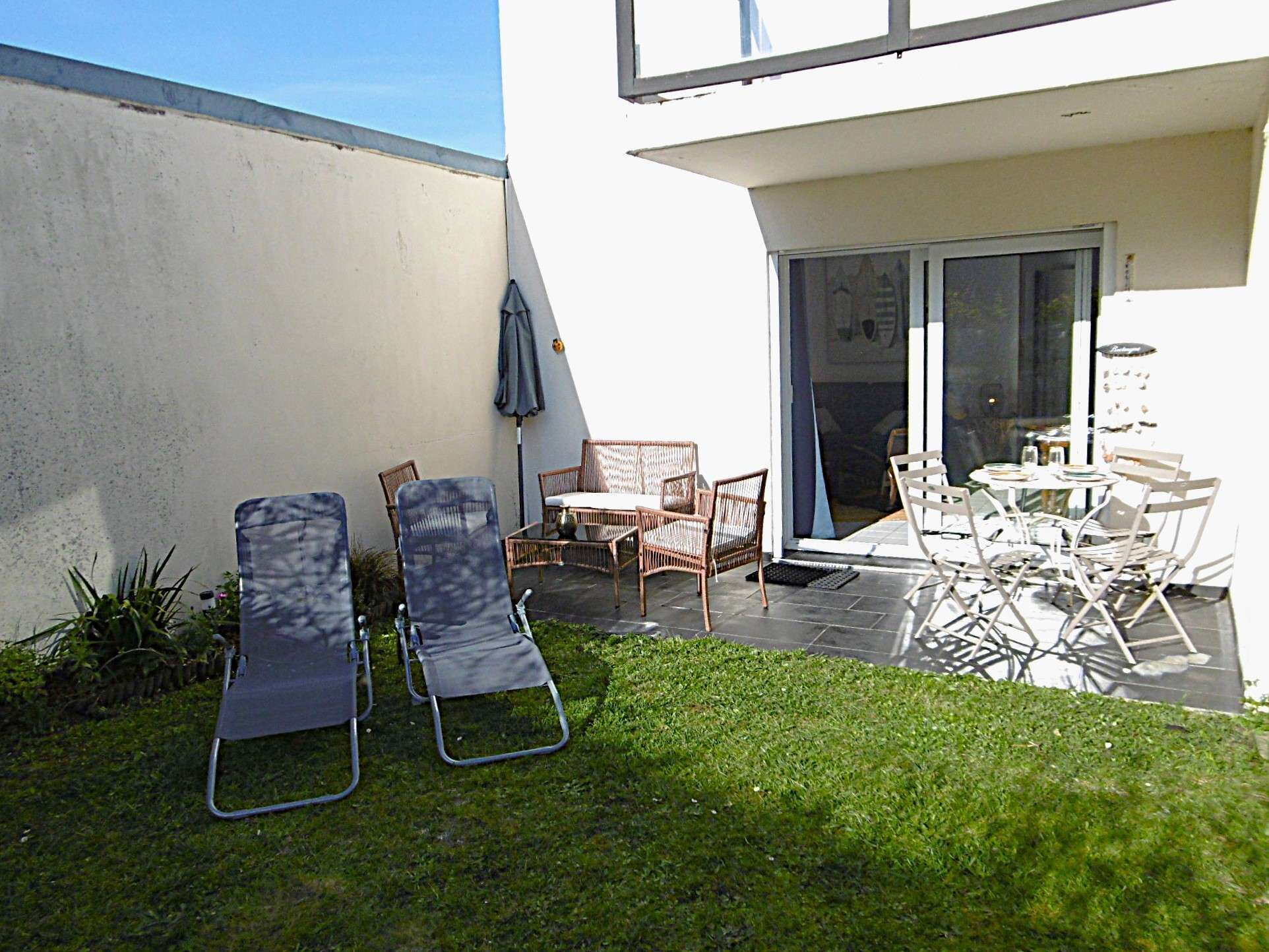 Eine Terrasse mit Gartenmöbeln, einer Glastür und einem kleinen Garten.