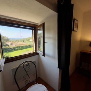 A room with a window overlooking a green landscape, a radiator, a metal chair, and a wooden cabinet. - Ancien moulin rénové avec piscine privée (OLMETO)