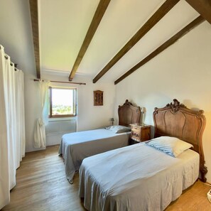 A bedroom with two beds, wooden beams, a window, and a small cabinet. - Ancien moulin rénové avec piscine privée (OLMETO)