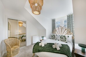 A bedroom with a bed, a chair, a bedside table, a mirror, and a window with curtains. - Ivory Court Suite - Grampian Lettings (Aberdeen)